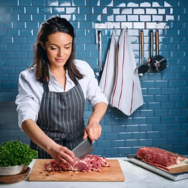 A chef finely mincing lamb and fat on a wooden cutting board for Adana Kebab.