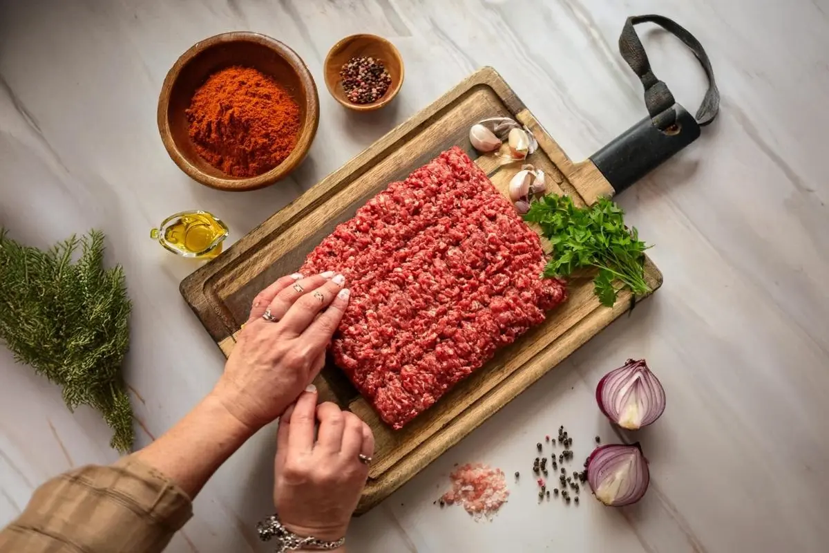 Key ingredients for Adana Kebab, including ground lamb, spices, and finely grated onion on a wooden cutting board.