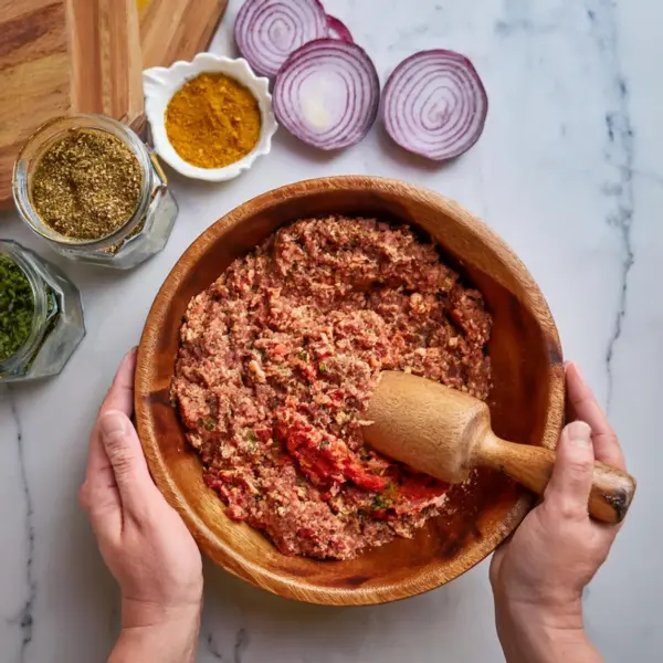 Ground lamb mixed with finely grated onion and Turkish spices in a wooden bowl for Adana Kebab preparation.