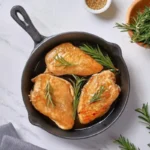 Chicken fillets cooking in a skillet with fresh rosemary.